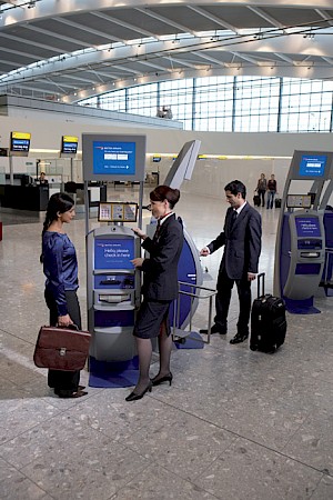 Samoobslužné kiosky s dotykovou obrazovkou jsou dobře viditelné v celé odletové hale. V pozadí přepážky Fast Bag Drop. - Autor: British Airways